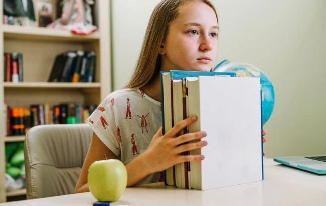 Дівчина вчителя за робочим куточком з книгами та глобусом