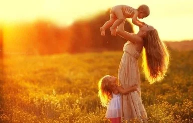 Мама піднімає дитину на руках, інша обіймає її ноги.