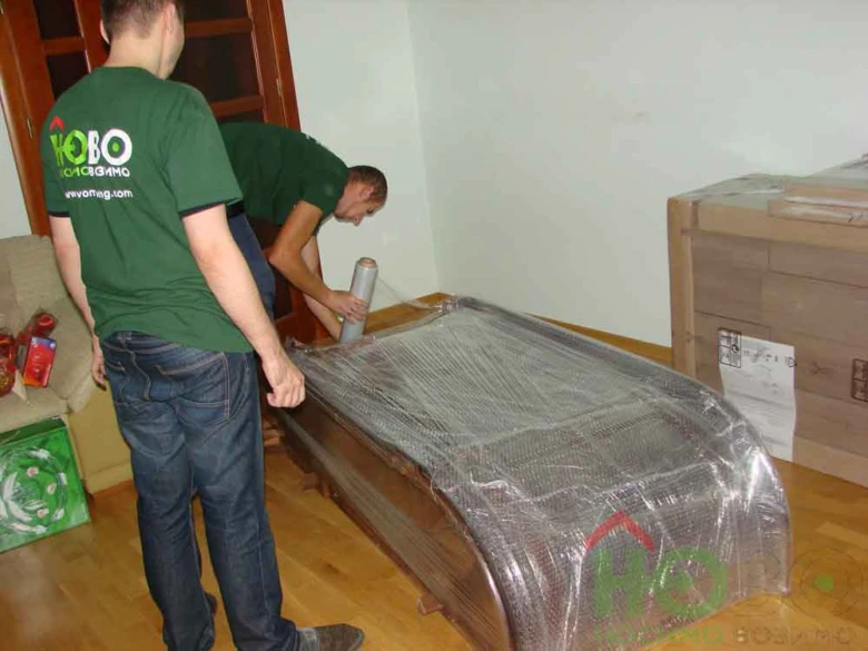 Два чоловіки обгортають меблі плівкою під час переїзду.