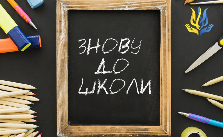 Чорна дошка з написом Знову до школи та шкільними приладдями.