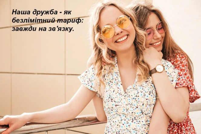 Дві подруги обіймаються на фоні світлої стіни.