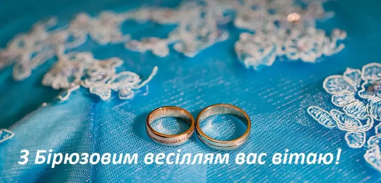 Два золоті кільця на блакитній тканині з привітанням.