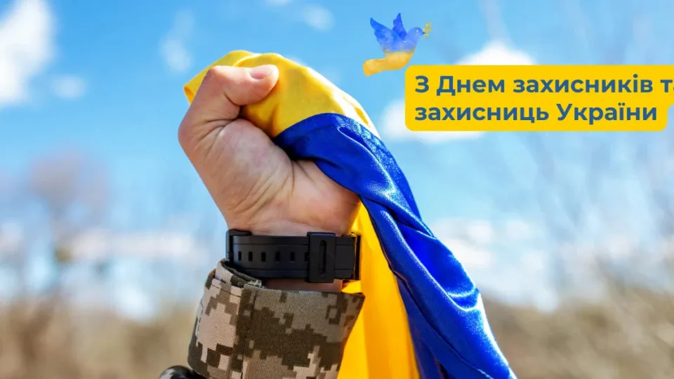Рука тримає український прапор на фоні неба.